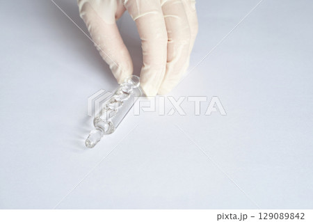 Gloved hand holding glass vial on white background in a laboratory setting Gloved hand holding glass vial on white background in a laboratory setting 129089842
