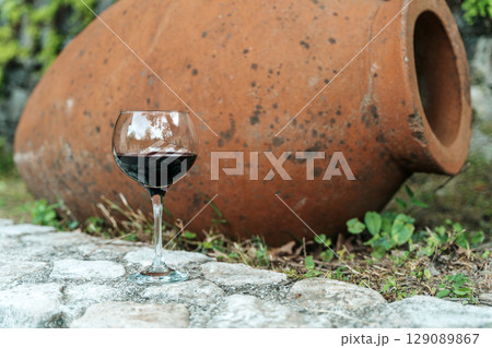 Glass of Red Wine with Traditional Georgian Qvevri in Rustic Setting Glass of Red Wine with Traditional Georgian Qvevri in Rustic Setting 129089867
