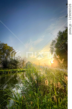 A Serene River at Sunrise Surrounded by Lush Greenery and a Beautiful Sky Full of Colors A Serene River at Sunrise Surrounded by Lush Greenery and a Beautiful Sky Full of Colors 129090326