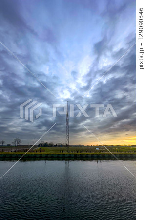 A stunning dramatic sky reflects beautifully over calm water, featuring a communication tower 129090346