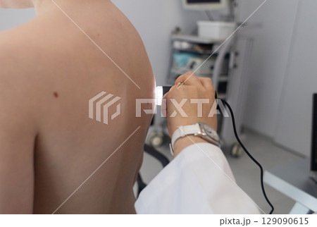A pediatric dermatologist examining a young boys skin with a dermatoscope in a medical clinic. Skin check up for moles and birthmarks. 129090615