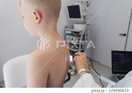 A pediatric dermatologist examining a young boys skin with a dermatoscope in a medical clinic. Skin check up for moles and birthmarks. 129090619