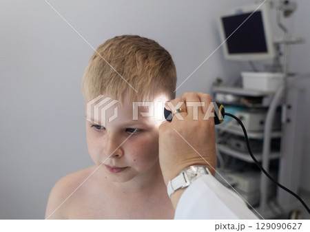 A pediatric dermatologist examining a young boys skin with a dermatoscope in a medical clinic. Skin check up for moles and birthmarks. A pediatric dermatologist examining a young boys skin with a dermatoscope in a medical clinic. Skin check up for moles and birthmarks. 129090627