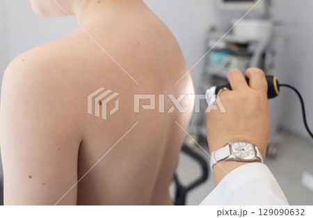 A pediatric dermatologist examining a young boys skin with a dermatoscope in a medical clinic. Skin check up for moles and birthmarks. 129090632
