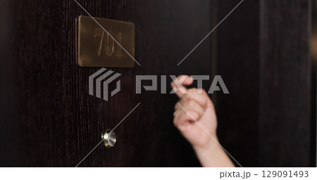Close-up woman hand knocking at the hotel door. Hotel staff member waking up tourist for breakfast. Hotel service. Close-up woman hand knocking at the hotel door. Hotel staff member waking up tourist for breakfast. Hotel service. 129091493