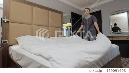 Hotel maid arranging white sheets, smoothing bedding while preparing room for incoming guests. Housekeeping service in hotel room. 129091498