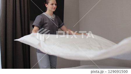 Chambermaid makes bed in hotel bedroom. Cleaning service in hotel rooms, hotel business. 129091500