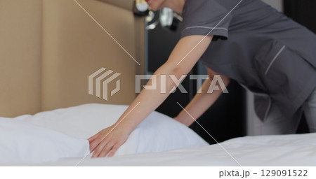 Housekeeper woman making bed and fluffing pillow in bedroom. Housekeeping service in hotel room. Housekeeper woman making bed and fluffing pillow in bedroom. Housekeeping service in hotel room. 129091522