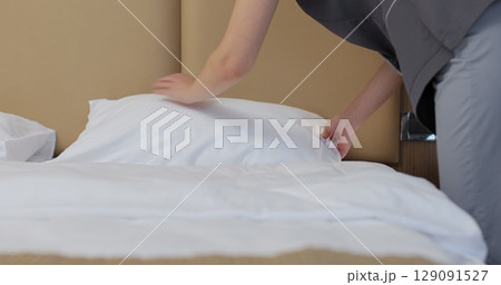 Close-up of young maid in uniform, fluffing pillows and punching them into shape. Hotel cleaning concept. Close-up of young maid in uniform, fluffing pillows and punching them into shape. Hotel cleaning concept. 129091527