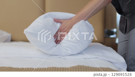 Close-up of young maid in uniform, fluffing pillows and punching them into shape. Hotel cleaning concept. 129091528