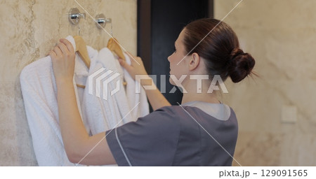 Female hotel maid changing fresh bathrobes in room. Cleaning service in hotel rooms, hotel business. 129091565