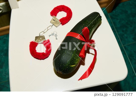 A Quirky Zucchini Styled with Handcuffs and a Colorful Ribbon on a Bathroom Floor 129091777