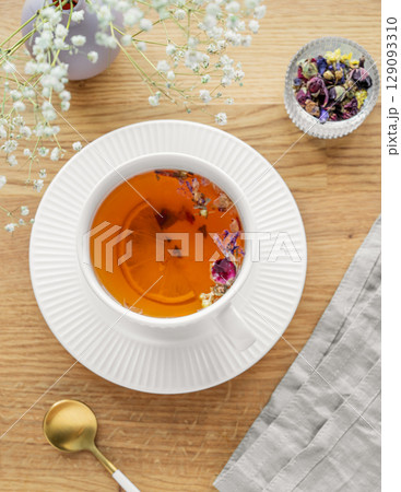A cup of herbal tea with lemon and bouquet of flowers on a wooden table with napkin. 129093310