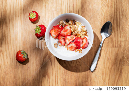 Granola or muesli with natural greek yogurt, strawberry and honey in a bowl on a wooden table 129093319