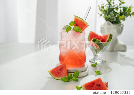 Watermelon mojito cocktail with ice and mint in a glass on a white table near window with slices Watermelon mojito cocktail with ice and mint in a glass on a white table near window with slices 129093333