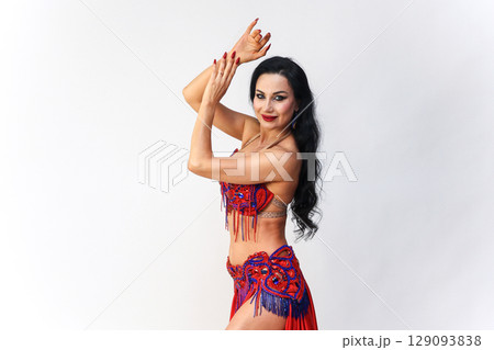 Brunette in Red Dress Performing Eastern Dance Movements Against a White Background 129093838