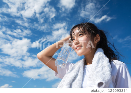 青空の下で水分補給する女性｜夏の爽快感と健康美を感じる一瞬 129093854