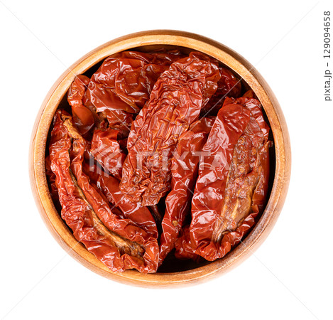 Sun-dried tomatoes, antipasto in a wooden bowl. Whole tomatoes, air dried under the Italian sun, treated with sea salt for preservation. Close-up, from above, isolated on white background, food photo. 129094658