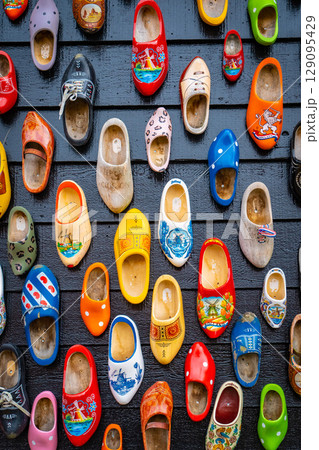Old wooden Dutch shoes - klomps. A lot of colorful old clomps against the background of a wooden wall. Popular souvenirs. Traditions of Holland. Background Old wooden Dutch shoes - klomps. A lot of colorful old clomps against the background of a wooden wall. Popular souvenirs. Traditions of Holland. Background 129095429