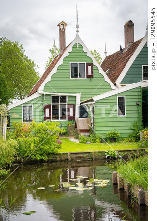 Dutch typical landscape. Traditional old dutch windmill with old houses against blue cloudy sky in the Zaanse Schans village, Netherlands. Famous tourism place. Sheep grazing on green grass. Dutch typical landscape. Traditional old dutch windmill with old houses against blue cloudy sky in the Zaanse Schans village, Netherlands. Famous tourism place. Sheep grazing on green grass. 129095545