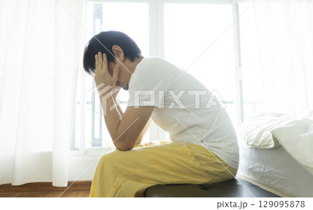 Adult Asian man sitting and feeling depressed on bed. Depression and loneliness concept. Adult Asian man sitting and feeling depressed on bed. Depression and loneliness concept. 129095878
