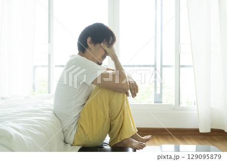 Adult Asian man sitting and feeling depressed on bed. Depression and loneliness concept. Adult Asian man sitting and feeling depressed on bed. Depression and loneliness concept. 129095879