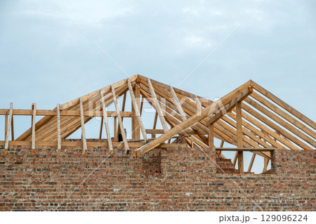 Building site with unfinished brick house with wooden roofing frame for future roof under construction. 129096224
