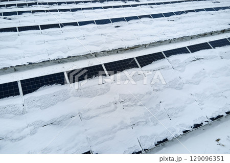 Aerial view of sustainable electrical power plant with solar photovoltaic panels covered with snow in winter for producing clean energy. Concept of low effectivity of renewable electricity in north 129096351