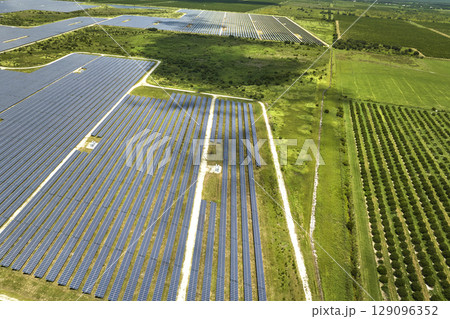 Aerial view of sustainable electric power plant between agricultural farm fields with solar photovoltaic panels for producing clean electrical energy. Renewable electricity with zero emission concept Aerial view of sustainable electric power plant between agricultural farm fields with solar photovoltaic panels for producing clean electrical energy. Renewable electricity with zero emission concept 129096352