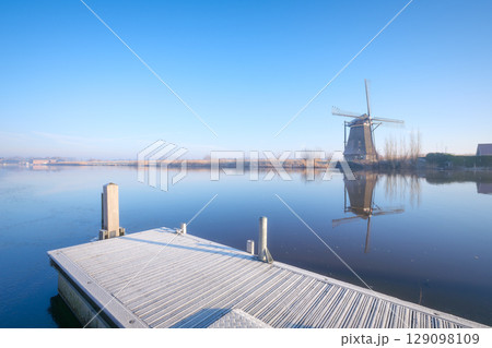 Windmill in the Netherlands during sunrise. Foggy morning and sunshine. Dutch canals. Windmill in the Netherlands during sunrise. Foggy morning and sunshine. Dutch canals. 129098109