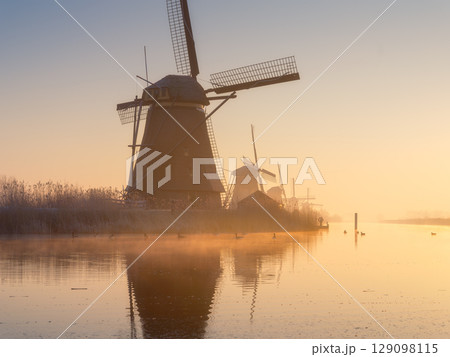 Windmills in the Netherlands during sunrise. Foggy morning and sunshine. Dutch canals. Windmills in the Netherlands during sunrise. Foggy morning and sunshine. Dutch canals. 129098115