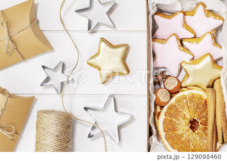 Hande made presents with home made cookies, dry fruits, nuts and cinnamon stiks on a white wooden background. Winter holiday pastries. Christmas cookies. Hand made gifts. Flat lay 129098460