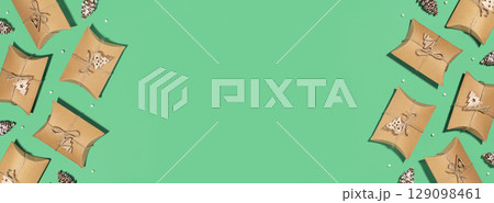 Christmas eco friendly banner. Craft gift boxes with decoration on a green background with empty place for text. Christmas, winter holiday, new year concept. Flat lay, copy space, banner size 129098461