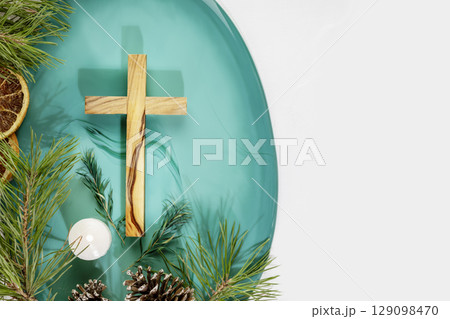 Wood cross laying on a green marble podium with fir branches, cones, candle and dry oranges on a white background with copy space. Christmas holidays. Christian religion card. Flat lay 129098470