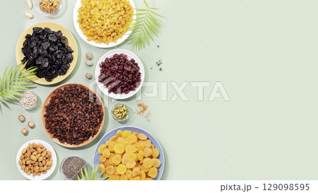 Natural dry fruits, nuts and seeds assortment on a blue background with palm leaves and copy space. Healthy snack - mix of organic nuts and dry fruits. Vegan and vegetarian products. Flat lay 129098595