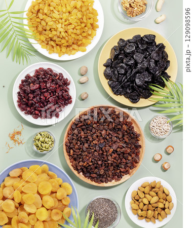Dry fruits, nuts and seeds assortment on a blue background with palm leaves. Healthy snack - mix of organic nuts and dry fruits. Vegan and vegetarian products. Flat lay Dry fruits, nuts and seeds assortment on a blue background with palm leaves. Healthy snack - mix of organic nuts and dry fruits. Vegan and vegetarian products. Flat lay 129098596