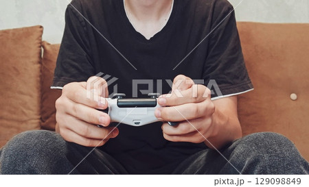 Joystick in hand: a person spends time playing games, a relaxed position. Gaming focused relaxation. silhouette of a man - a teenage boy playing a video game. Joystick in hand: a person spends time playing games, a relaxed position. Gaming focused relaxation. silhouette of a man - a teenage boy playing a video game. 129098849