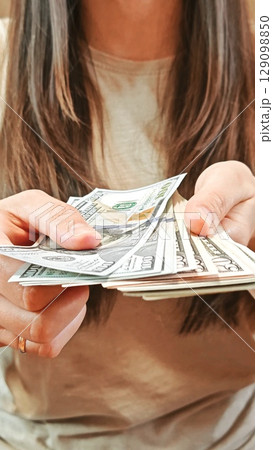 Unrecognizable woman counting US dollar bills. Counting cash bills. 100 USD. Display of US dollar bills in hand. Unrecognizable woman counting US dollar bills. Counting cash bills. 100 USD. Display of US dollar bills in hand. 129098850