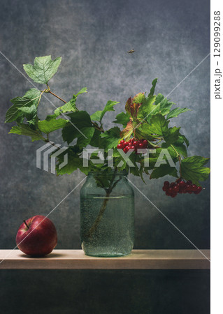 Apple and a branch of red viburnum in a glass jar with water Apple and a branch of red viburnum in a glass jar with water 129099288