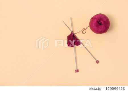 Vinous knitted wool on orange background with knitting needles for knitting warm clothes and hobbies needlework Vinous knitted wool on orange background with knitting needles for knitting warm clothes and hobbies needlework 129099428