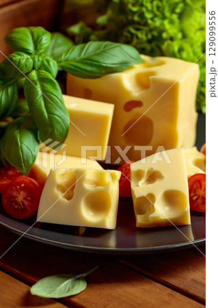 Swiss cheese, green basil, salad, and tomatoes on a wooden table. Swiss cheese, green basil, salad, and tomatoes on a wooden table. 129099556