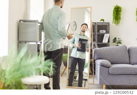 Practicing or rehearsing man looking attentively at his reflection in full-length mirror to prepare  129100532