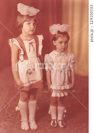 Two sisters with bows in Soviet times take a photo in a studio in 1986 Two sisters with bows in Soviet times take a photo in a studio in 1986 129100583
