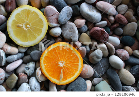 Two halves of ripe lemon and fresh orange on a sea stones at a side of image concept for logo or titles 129100946