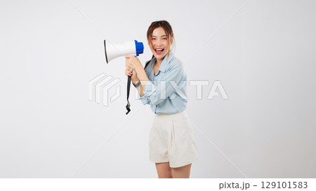 A young Asian woman is shouting into a megaphone, making an important announcement. Her mouth is wide open, actively screaming the news through her reliable megaphone. isolated studio white background 129101583