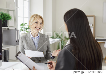Two cheerful female business people sitting at the desk in modern office working with documents Two cheerful female business people sitting at the desk in modern office working with documents 129101886
