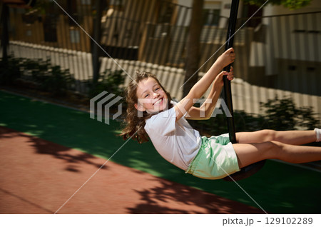 Smiling Child Enjoying a Swing Ride in a Sunny Playground Smiling Child Enjoying a Swing Ride in a Sunny Playground 129102289