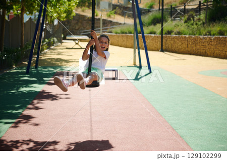 Young Girl Joyfully Swinging on a Playground Rope During Summer 129102299