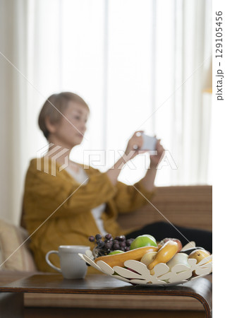 ソファーに座りスマホを手にする高齢女性 129105456