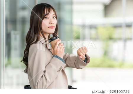 オフィスビルの前で待ち合わせをする若いアジア人ビジネスウーマン（腕時計,スケジュール,デート） 129105723